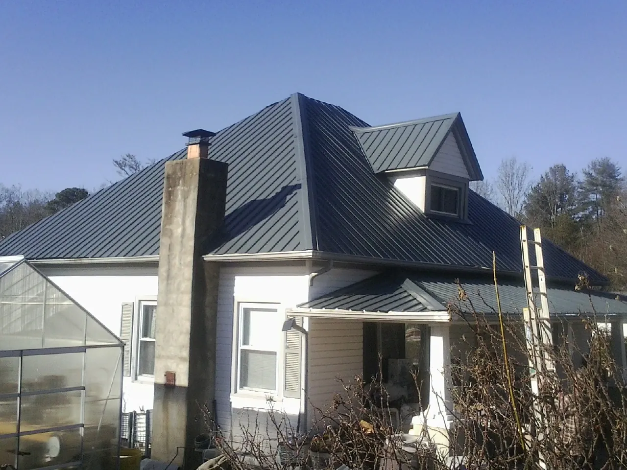 Dark blue standing seam metal roof on a white farmhouse with dormer — Slate & Tile Roof Repair by Roofing Brothers in Spencer